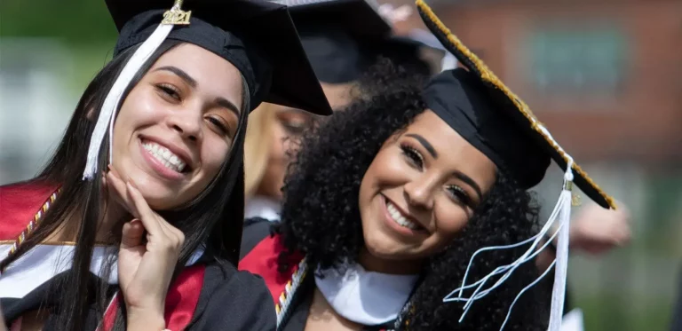 Two women graduates posing with smiles.